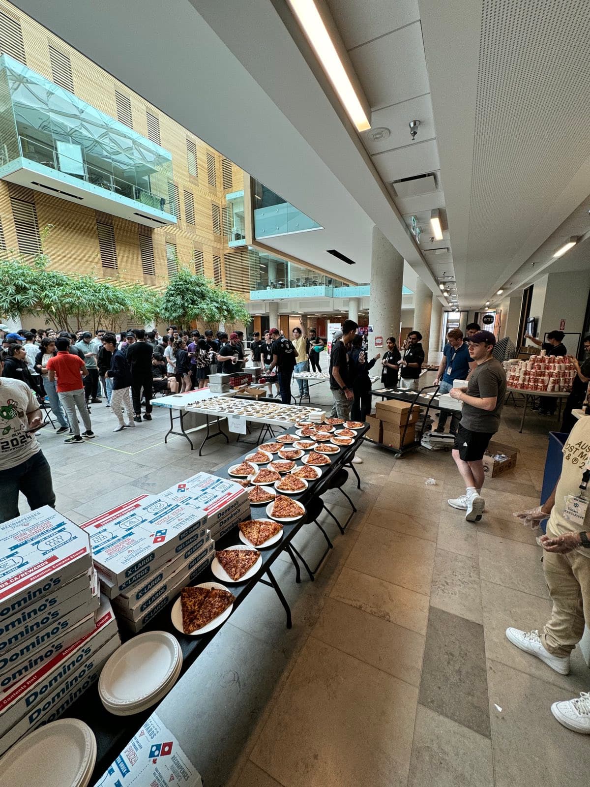 Hackers lining up for pizza in a university atrium at HawkHacks 2024