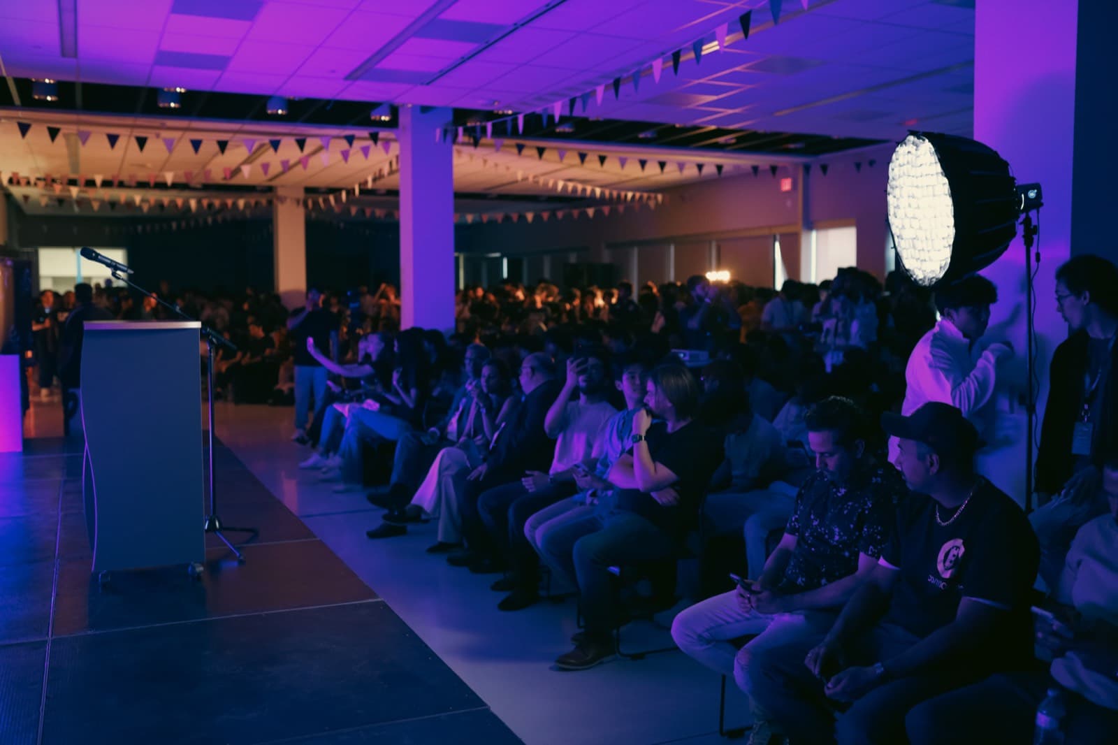 The SpurHacks 2025 audience under violet stage light